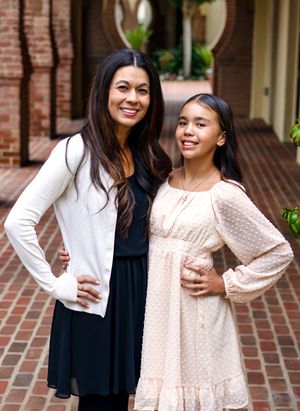 two women in coordinating pink and black dresses stand together in a brick courtyard setting.