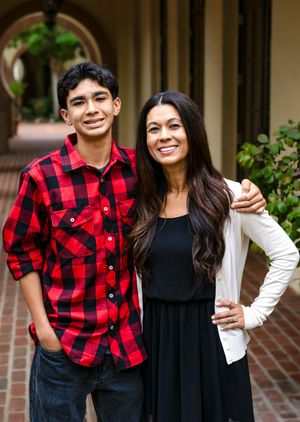 A couple wearing coordinating red buffalo plaid and black outfits pose together outdoors by a brick wall.