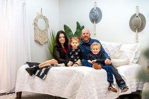 Cozy indoor family portrait on white bed with macrame wall decor and neutral tones.