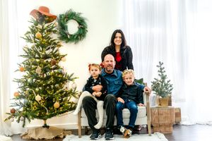 Christmas family portrait by decorated tree with wreath and rustic holiday decor.