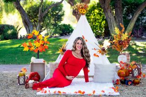 Outdoor maternity session with white teepee, fall decorations and pumpkins on blanket.