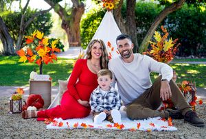Family maternity photos on blanket with teepee and autumn decorations in outdoor setting.