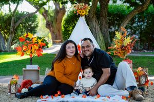 Fall family photoshoot with white teepee tent, orange maple leaves and lantern decorations in garden setting.