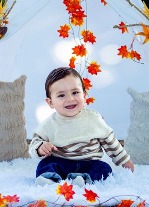 Autumn themed portrait with orange maple leaves falling around white teepee tent and cozy pillows.