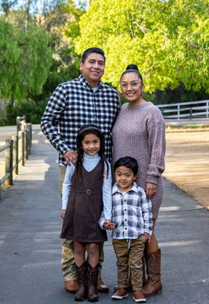 Family in coordinated casual outfits posing on paved walkway with autumn trees in background.