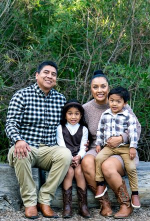 Family sitting together on rustic bench wearing coordinated casual outfits in natural setting.