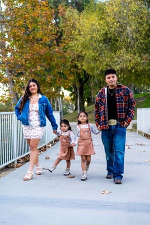 Family wearing coordinated plaid shirts and denim walk together on a path surrounded by autumn trees.