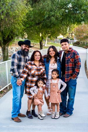 Group in matching plaid shirts and denim pose together on a concrete walkway with trees in background.
