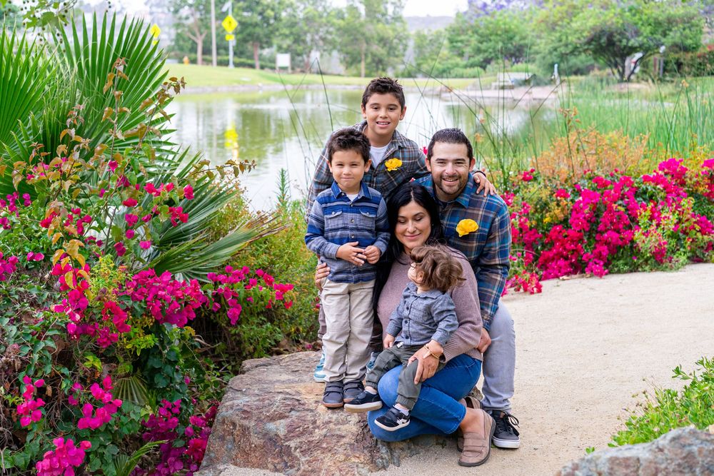 Family of four posing among colorful flowers by a pond in a lush garden park.