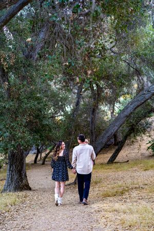 Couple strolling hand in hand down a scenic trail surrounded by trees.