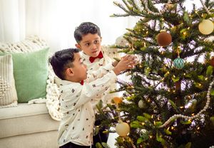 Two children decorating Christmas tree with gold ornaments and lights.