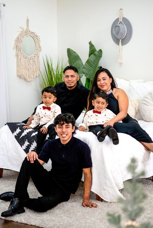 Indoor family portrait on white couch with boho wall decor and tropical plants.