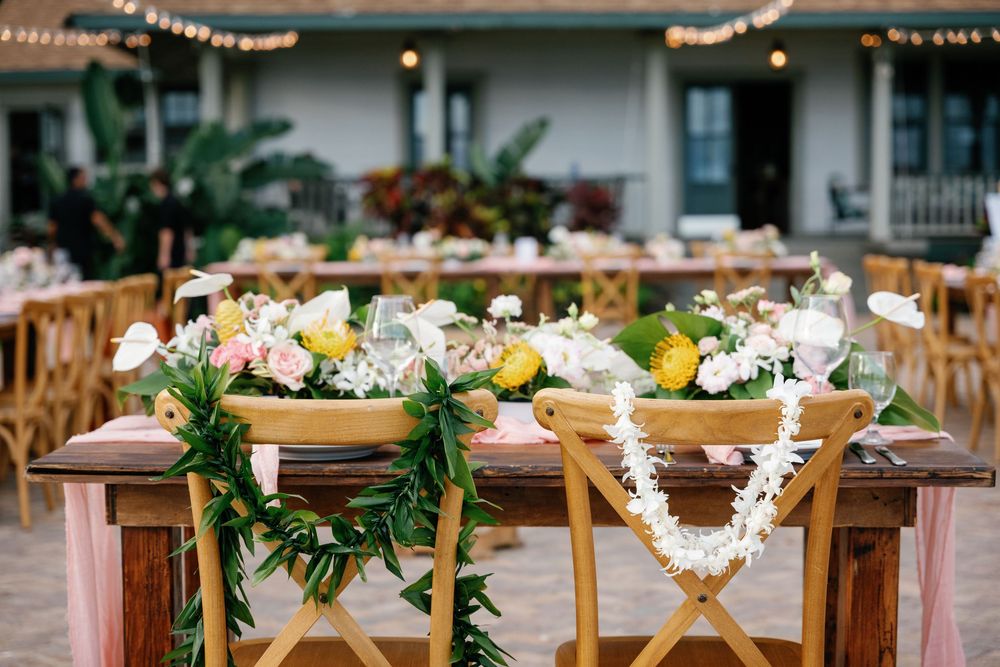 Olowalu Plantation House reception with wooden tables, floral centerpieces, & greenery garlands.