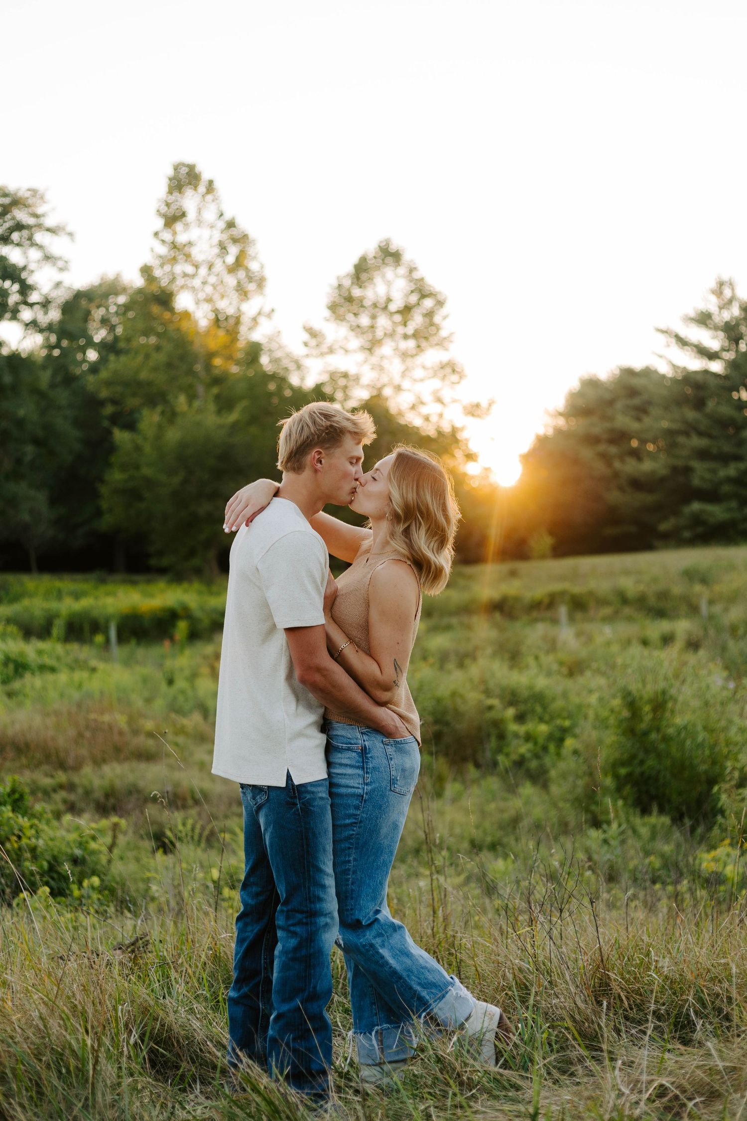 A sweet candid moment between a couple in casual clothing standing in a sunny meadow.