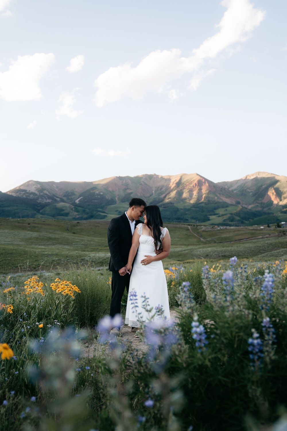 Couple embracing in a wildflower meadow with mountain backdrop during golden hour engagement session in Colorado.