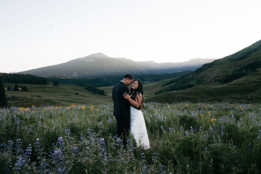 Couple embracing in a wildflower meadow with mountain backdrop at sunset during their outdoor wedding.