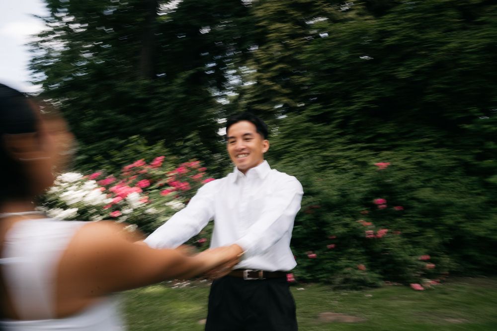 Groom in white shirt smiling warmly at bride during outdoor wedding shoot with blooming roses behind him.