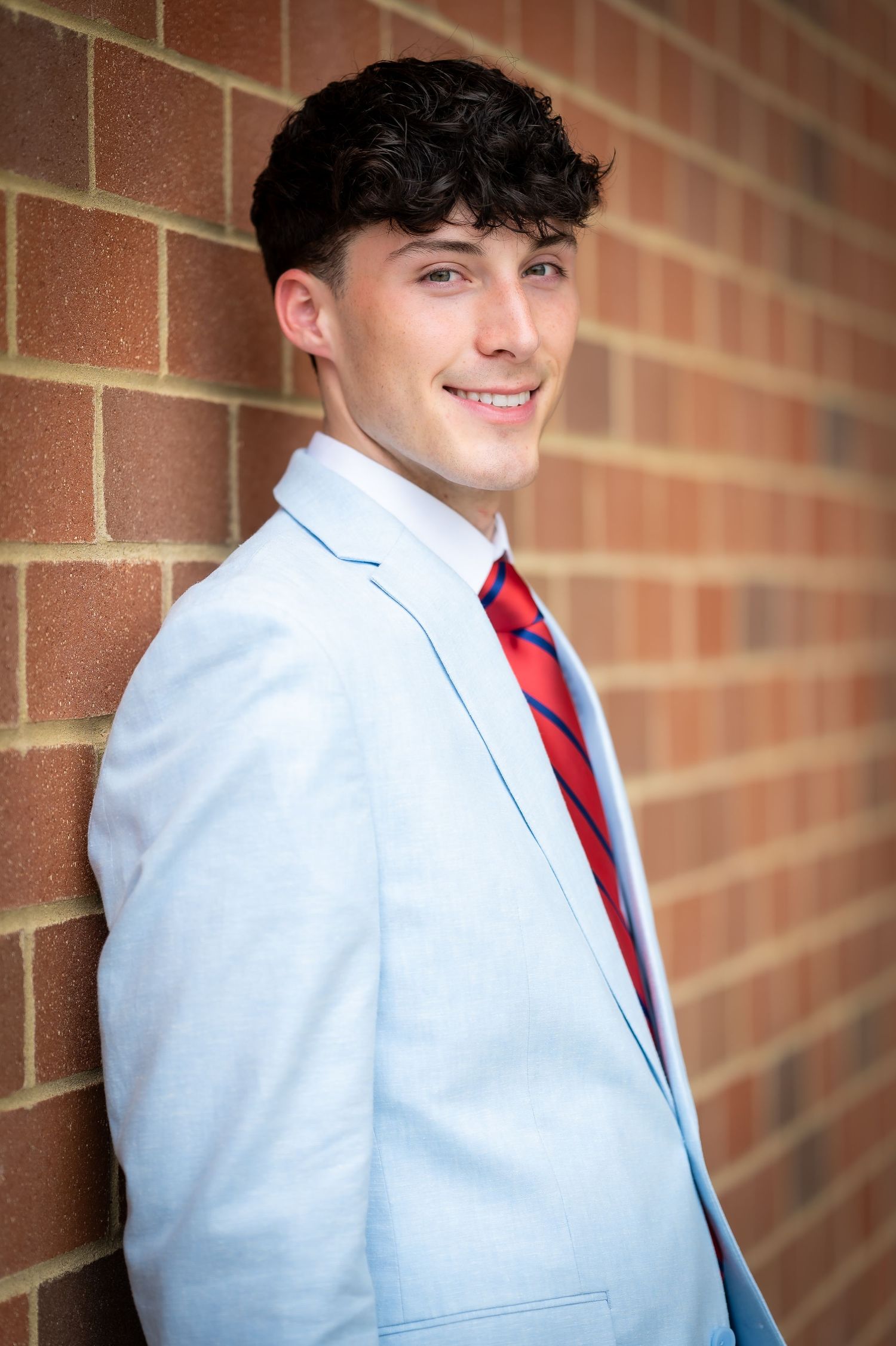 White formal suit jacket with red tie photographed against a brick wall background.