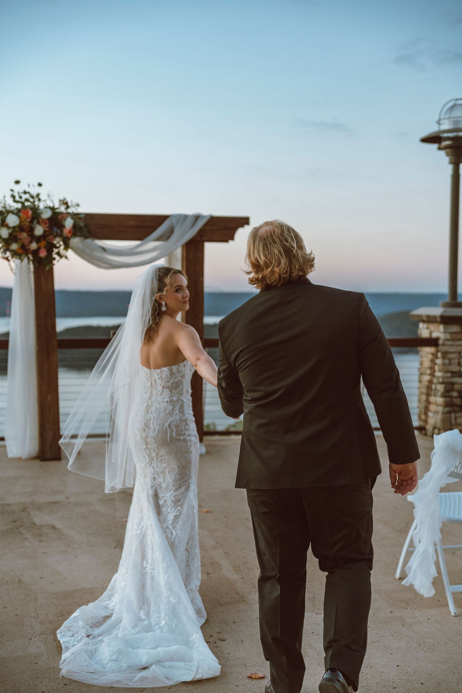 A couple in formal wedding attire shares a moment at an outdoor waterfront venue.