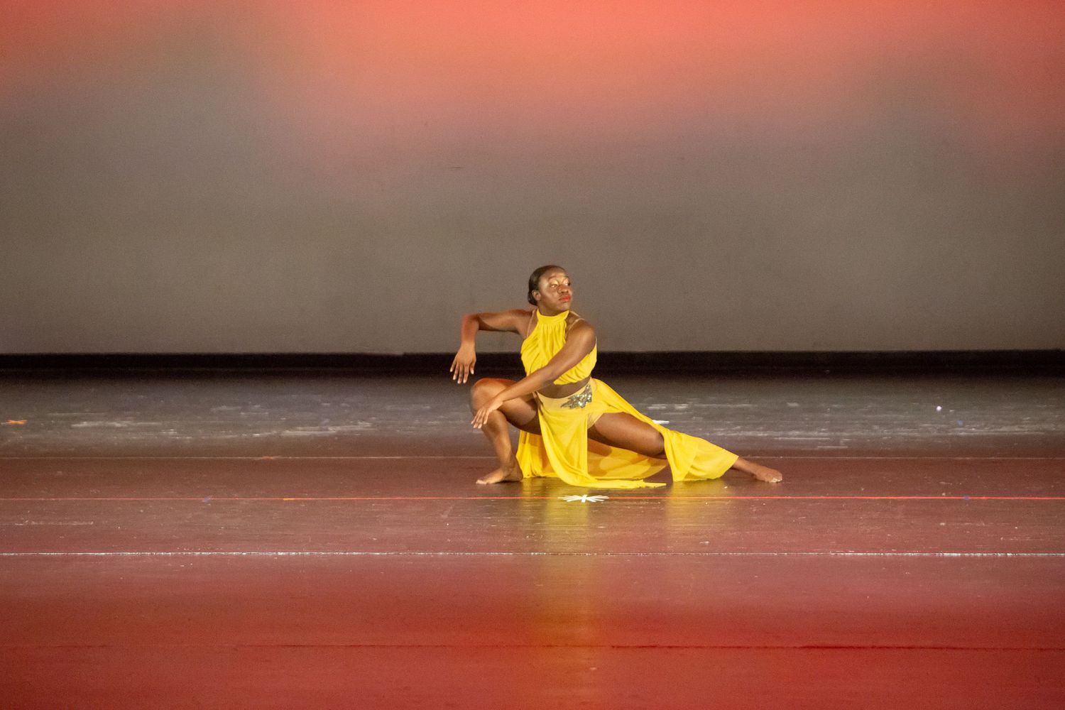 Graceful dance performance in yellow costume on stage with red lighting.