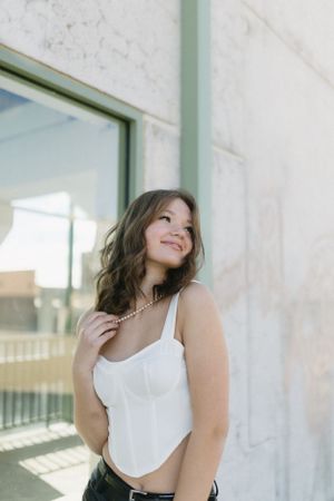 A woman in a white crop top poses against a sunlit wall with natural lighting.