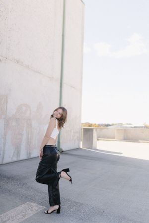 Playful urban fashion pose against concrete wall in sunlight.