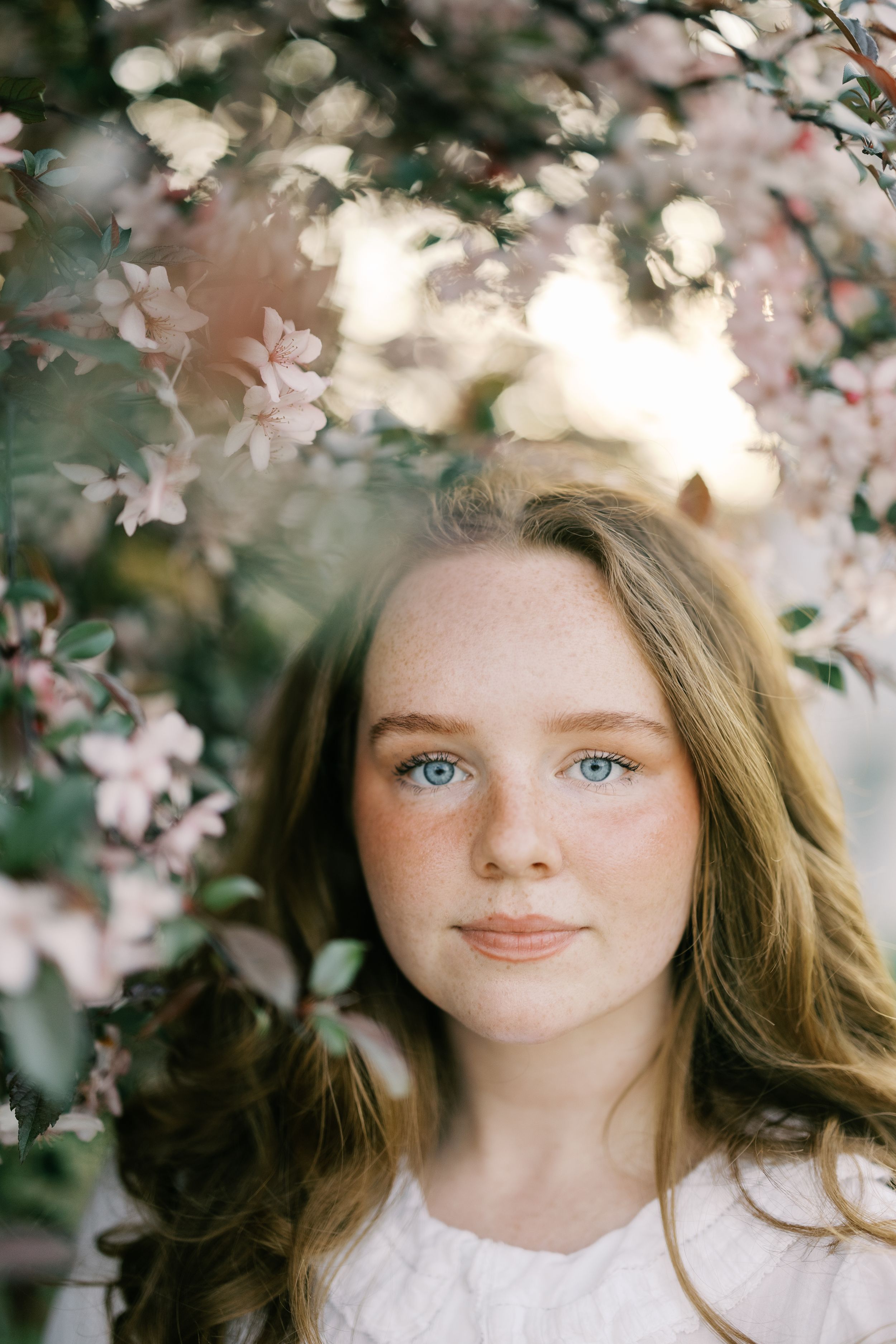 Portrait of a young woman with striking blue eyes amid delicate cherry blossoms in spring.