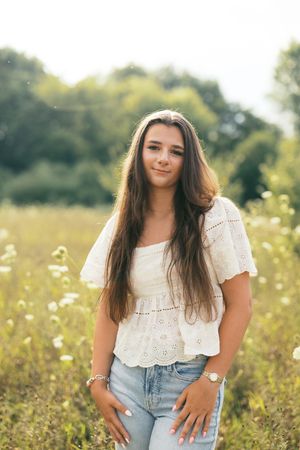 A person wearing a white eyelet lace top and jeans poses in a sunny wildflower meadow during golden hour.