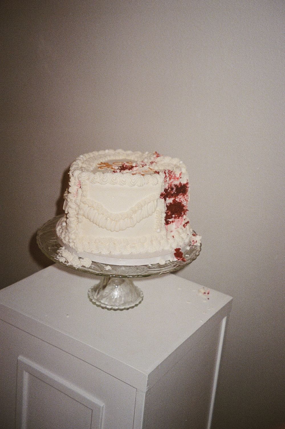 A white wedding cake with red velvet interior sits on a glass cake stand.