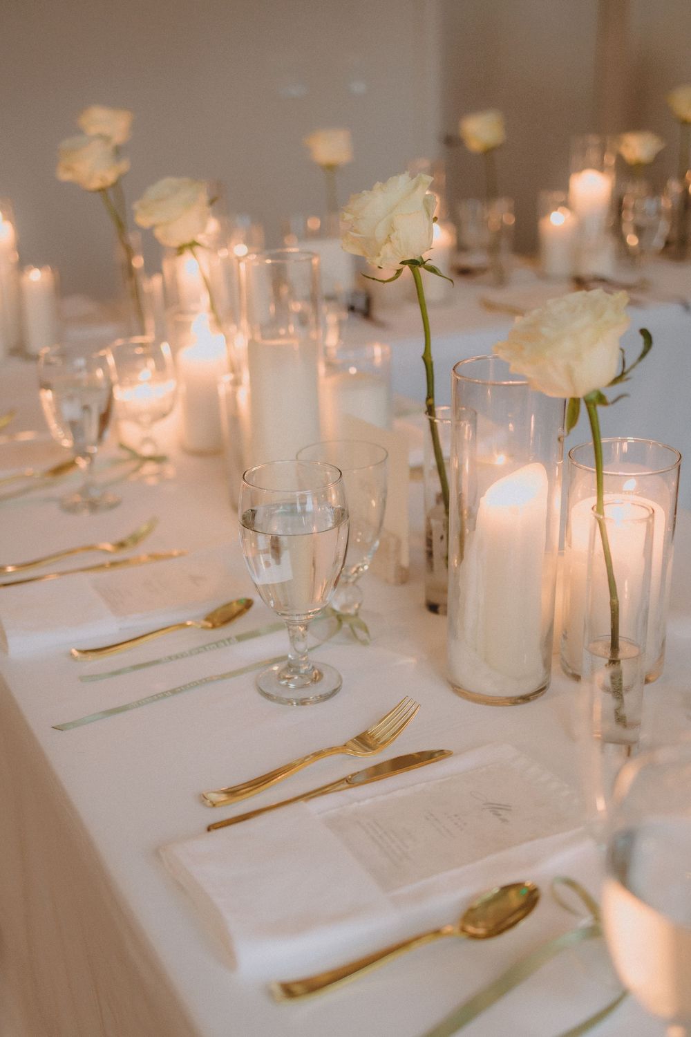 Elegant wedding reception table settings with white linens, gold flatware, and glowing candles create a romantic atmosphere.