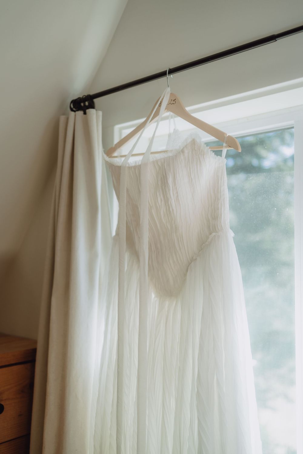 White wedding dress hanging on display near a window with natural light.