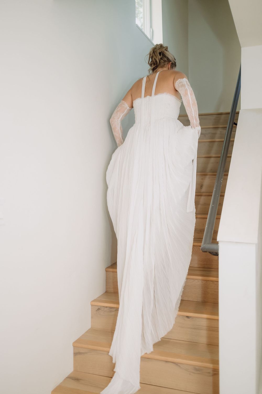 Back view of bride in flowing white dress ascending wooden stairs.