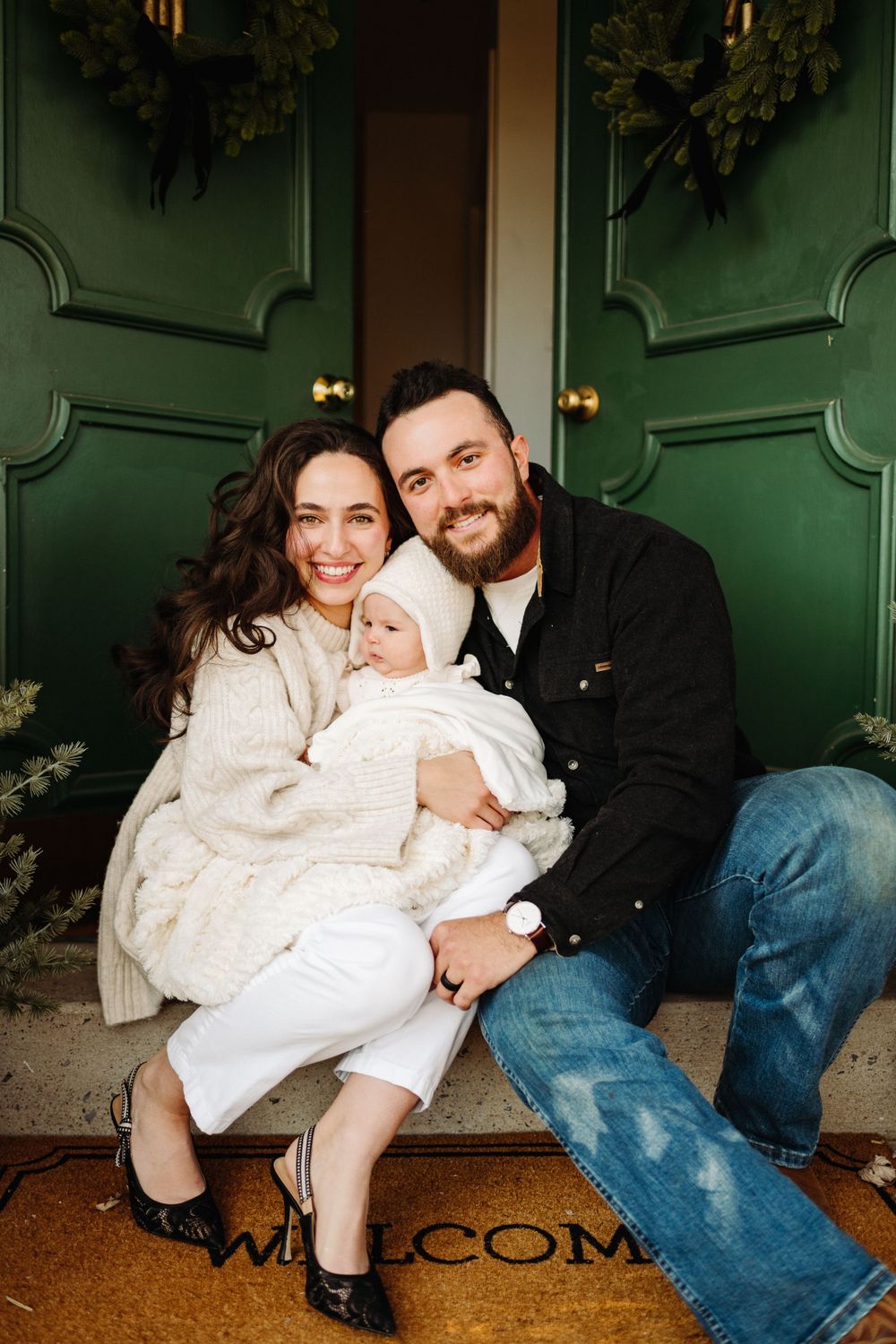 Family sitting on doorstep with holiday wreaths and green doors.
