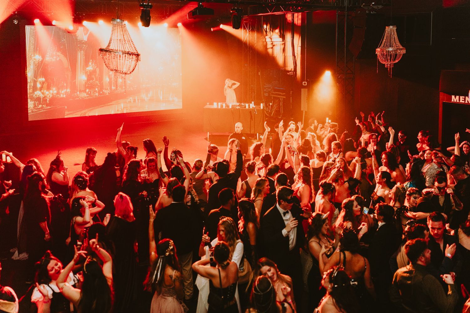 Crowded concert venue bathed in dramatic red lighting with silhouetted audience.