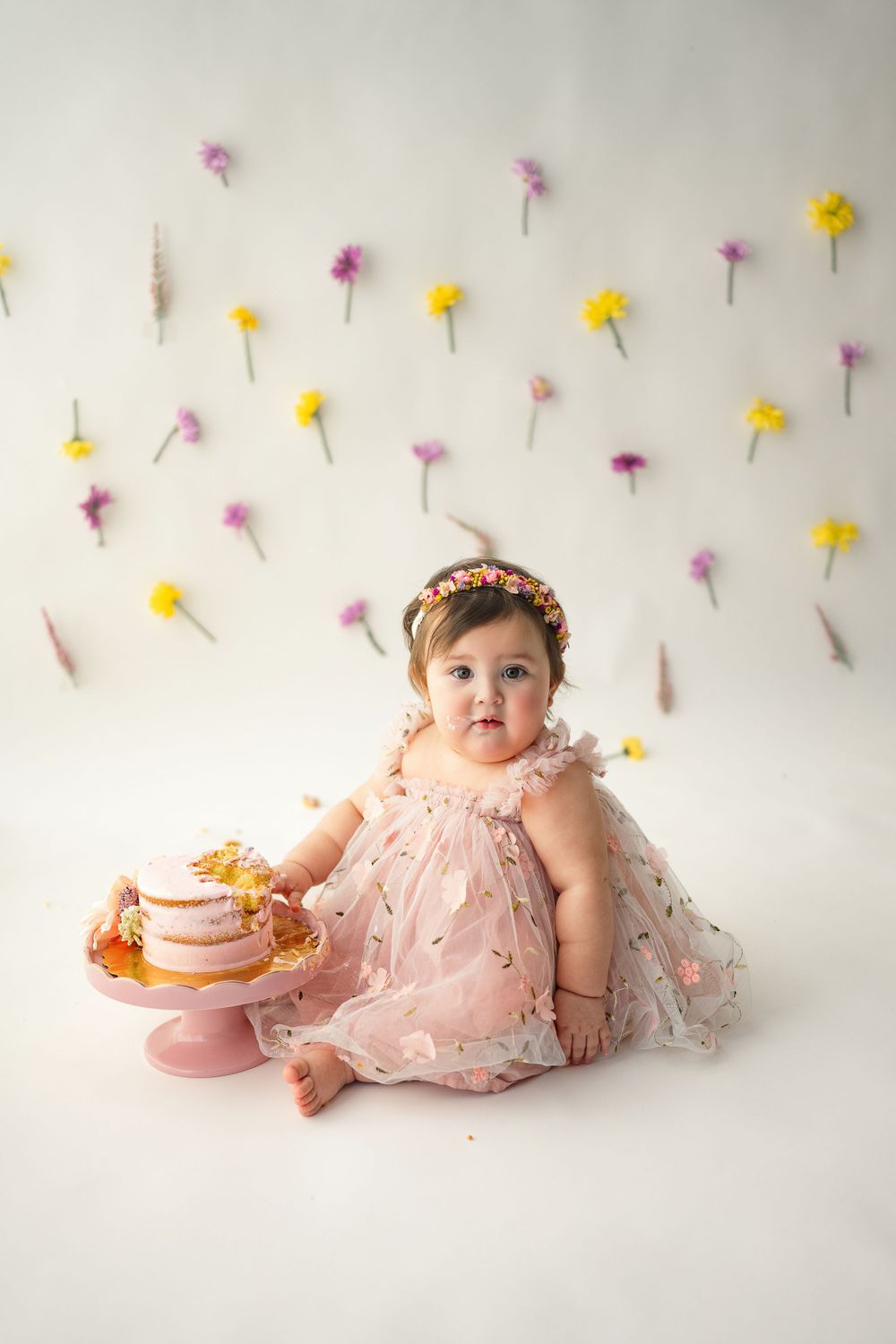 Baby girl with brown hair and bright eyes looks at camera in cake smash first birthday portraits photography session in Clarksville studio