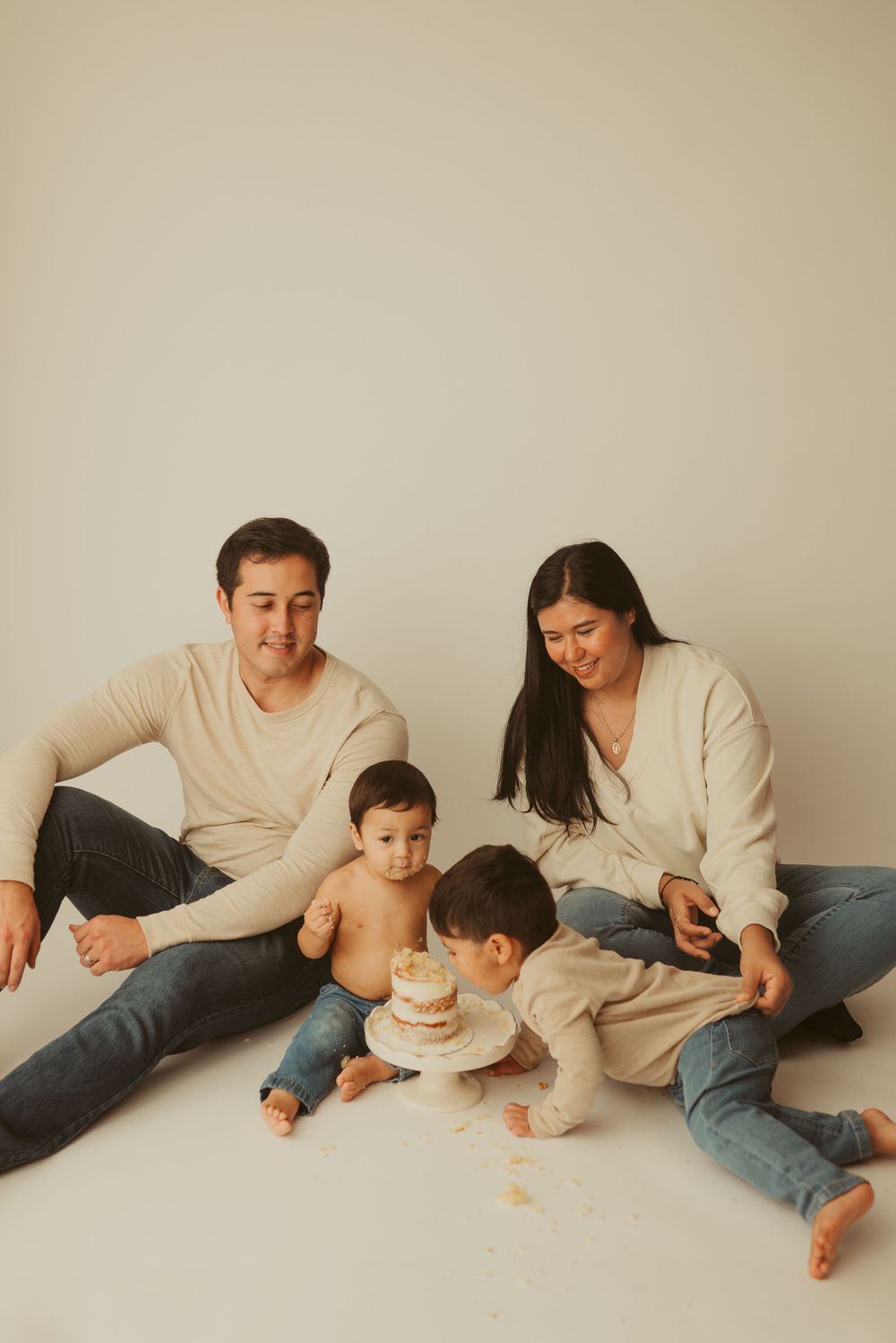 Family of 4 joins in on baby's cake smash session on minimalist backdrop in Clarksville, Tennessee photography studio.
