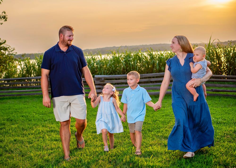 A family walks together on a grassy hilltop at sunset with a cornfield in the background.