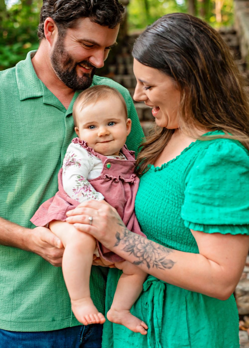 Family in coordinating green and pink outfits share tender moments together outdoors during a photo session.