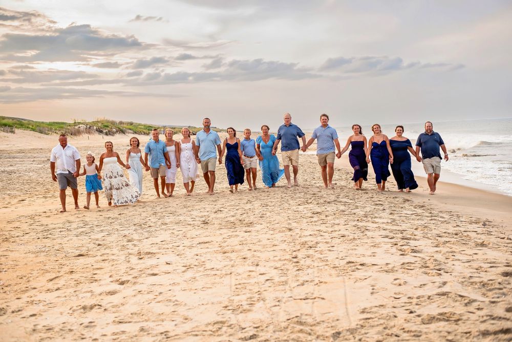Large family group walking together on a sandy beach at sunset, dressed in coordinating blue and white outfits.
