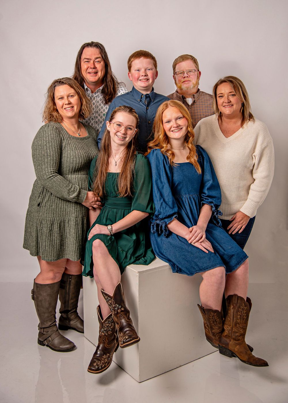 A group sits casually together in coordinated outfits of green and blue against a neutral studio backdrop.