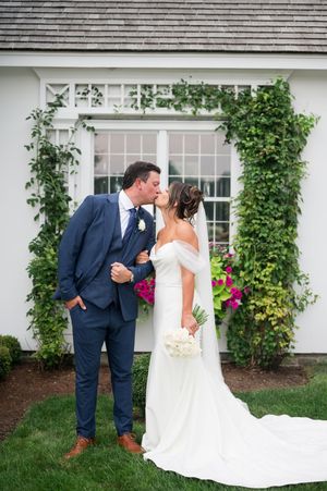 Romantic wedding couple shares intimate moments against white building with climbing vines and flowers. Smith Farm Garden CT