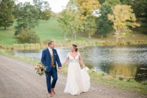 Newlyweds walk together near autumn pond in outdoor garden setting.