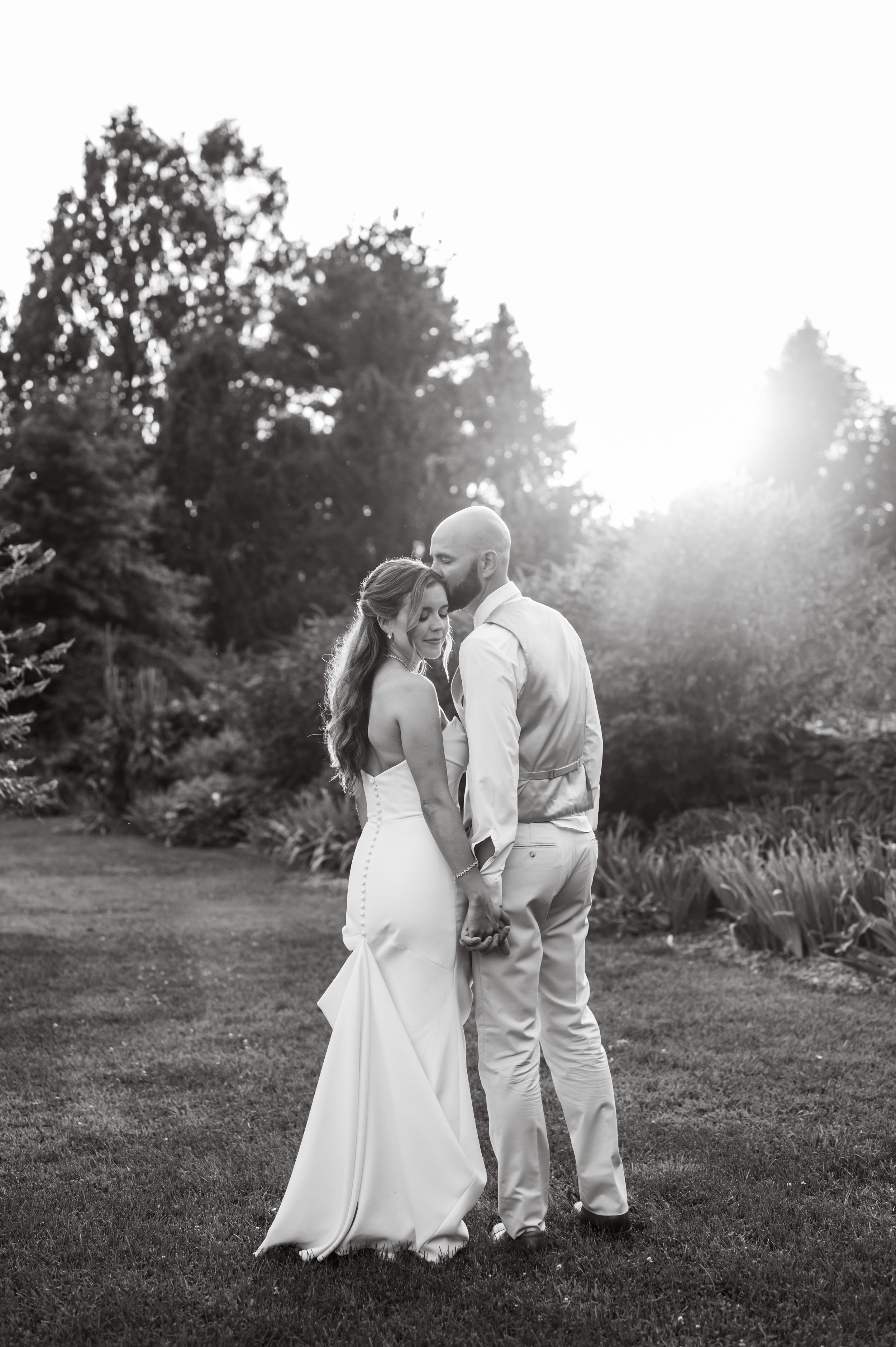 A romantic black and white portrait of a couple embracing in a sunlit garden setting at Kalmia Garden at Gastler Farm
