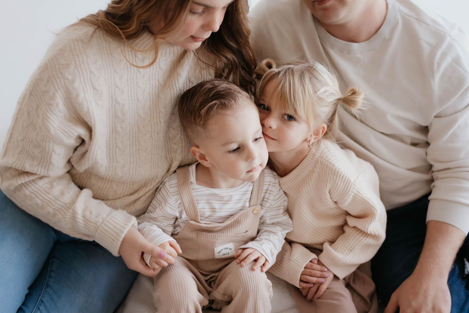 A family wearing neutral colored sweaters sits together in a cozy indoor portrait session in a studio in Colorado Springs