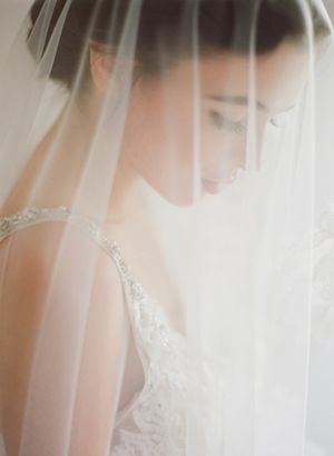 Ethereal bridal portrait of bride in lace gown draped beneath soft flowing white wedding veil.