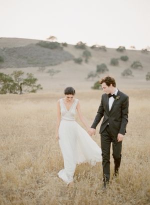 Bride and groom holding hands walking through golden field at sunset wedding photography.