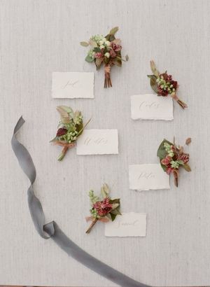 Rustic wedding place cards with floral boutonnieres and gray ribbon flat lay.