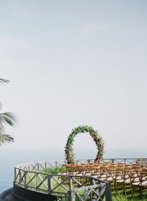 Elegant outdoor wedding ceremony setup with floral arch overlooking the ocean on a cliffside terrace.