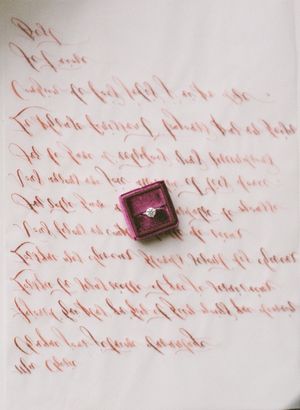 Romantic handwritten love letter in calligraphy with a diamond ring in a pink velvet box as centerpiece.