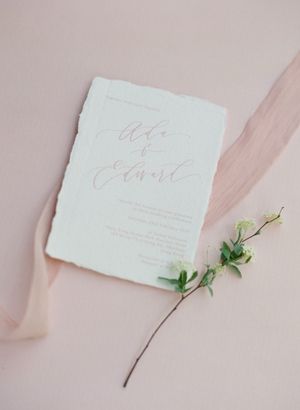 Elegant wedding invitation with calligraphy script on handmade paper with torn edges and a delicate green sprig.
